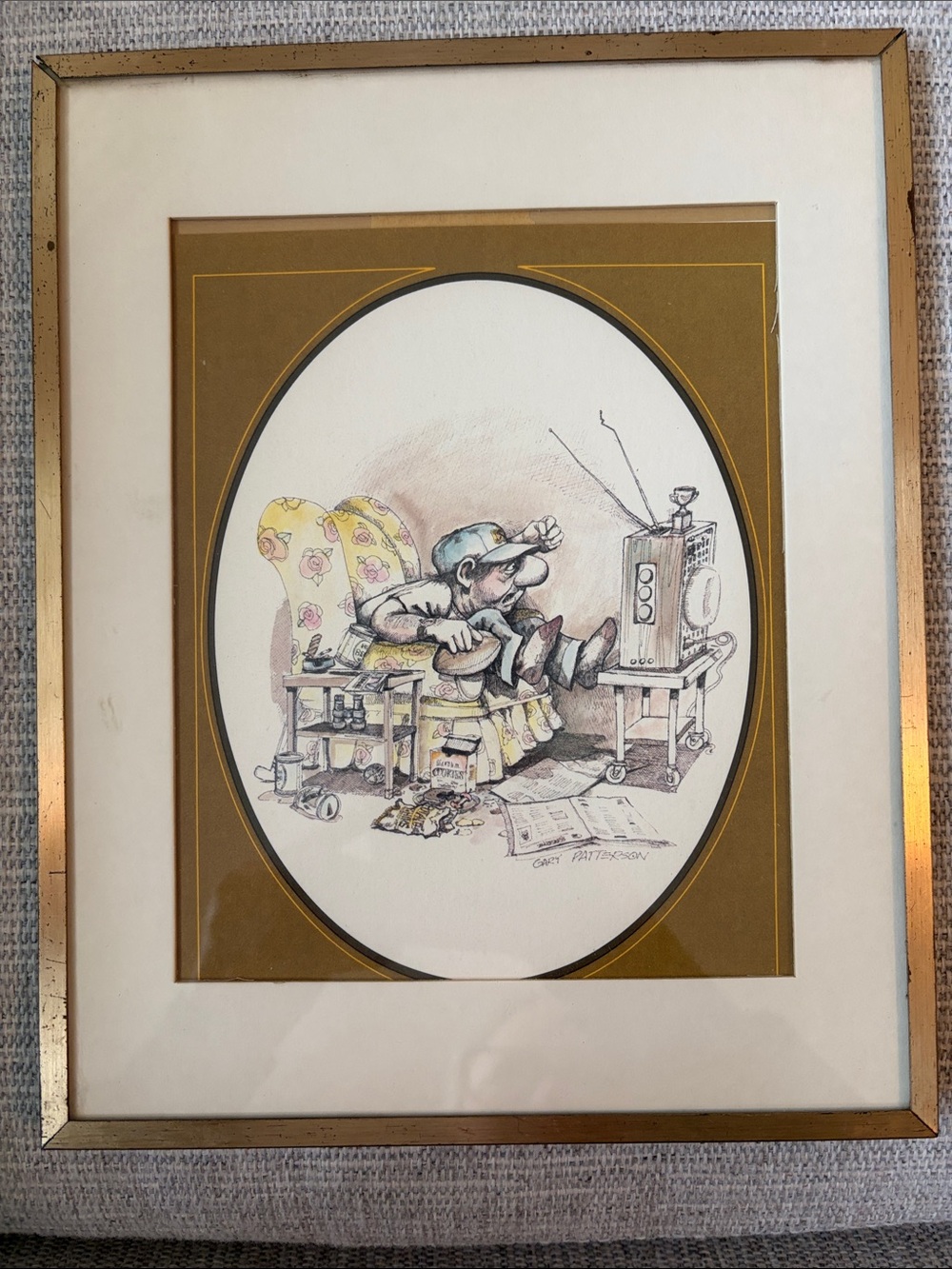 A humorous framed print by Gary Patterson w/ man watching television. 1975-1976